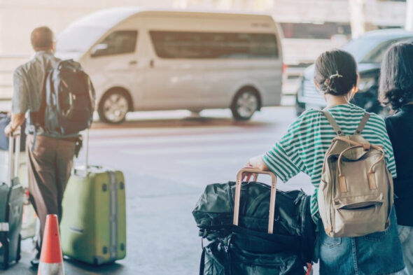 Passengers with big roller luggage stand to wait for the car to pick up at airport arrival terminal.